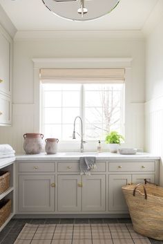 a kitchen with white cabinets and gray flooring, an open window above the sink