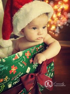 a baby wearing a santa hat sitting in a christmas present box with lights behind it