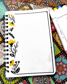 an open notebook sitting on top of a colorful table cloth covered with papers and markers