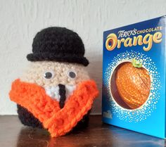 a crocheted orange with a hat and scarf next to a book on a table