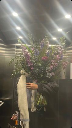 a man holding a bouquet of flowers in front of a mirror with lights on it