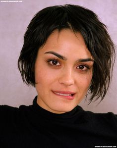 a close up of a person wearing a black shirt and posing for the camera with her hand on her shoulder