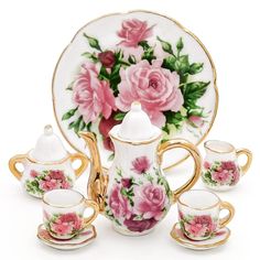 a porcelain tea set with pink flowers and gold trimmings on the front, sitting next to two matching cups and saucers