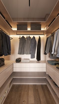 a walk in closet with clothes hanging on the wall and wooden flooring that is lit by recessed lighting