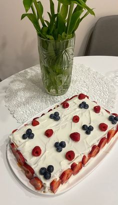 a cake with berries and blueberries on it sitting on a table next to a vase filled with flowers