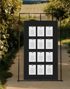 a black and white wedding seating chart is displayed on a metal frame in the middle of a path