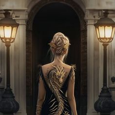 a woman in a black dress with gold designs on her body and back, standing outside an ornate building