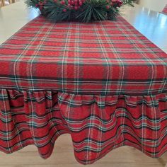 a red plaid table cloth on top of a dining room table with pine branches in the center