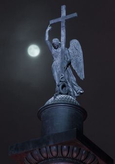 an angel statue holding a cross on top of a building with the moon in the background