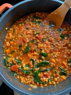 a wooden spoon in a pot filled with vegetables and lentulas on the stove