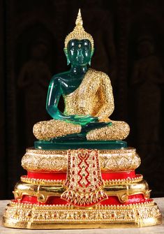 a green buddha statue sitting on top of a pile of red and gold items