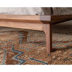 a close up of a wooden bed frame on a carpeted floor with an area rug in the background