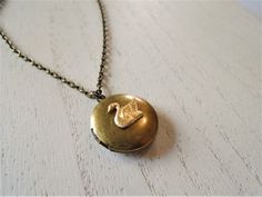 "A round brass locket with a swan on it is hanging from antiqued brass chain. The locket is a darkened brass and the swan is a made of raw brass giving it a golden color. You can select your length of chain at checkout. Locket measures approx. 1\" and opens to hold two small pictures. Necklace will come in a gift box and bow ready for gift giving. Enter back into store: rhondastreasures.etsy.com   RhondasTreasures" Swan Jewelry, Swan Necklace, Bird Necklace, Small Pictures, Golden Color, Locket Necklace, Brass Chain, Raw Brass, Beautiful Earrings