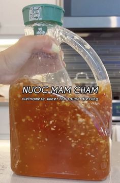 a person is holding a plastic bottle with liquid in it and the label on top reads nuoc - mam cham