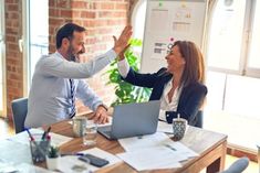 two business people giving each other high fives in front of a laptop computer on a table