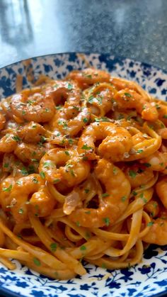 a blue and white bowl filled with pasta covered in sauce, shrimp and parsley