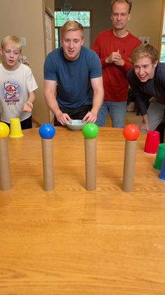 a group of people standing around a wooden table with colorful balls on top of it