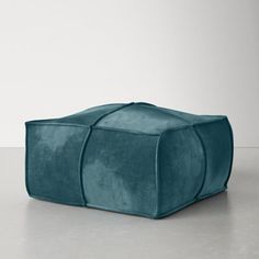 a blue velvet poufce on a white floor with an empty wall in the background