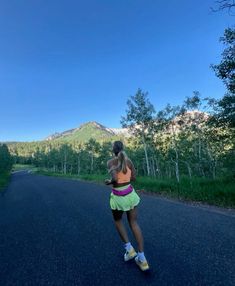 a woman is running down the road with mountains in the background