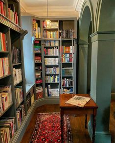 a room filled with lots of books next to a wooden table on top of a hard wood floor