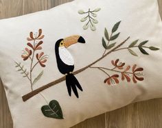 an embroidered pillow with a toucan bird on it's branch and leaves