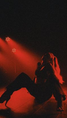 a woman sitting on the floor in front of red light with her legs spread out