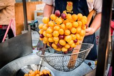 a man holding a bunch of oranges over a metal bowl on top of a table