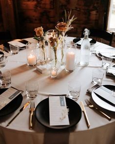 the table is set with white and black plates, silverware, candles and flowers