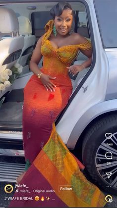 a woman in an orange and yellow dress standing next to a car