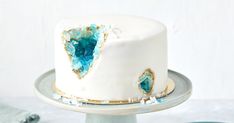 a white cake with blue and gold decorations on it's side sitting on a silver platter