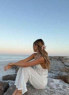 a woman sitting on top of a rock next to the ocean wearing a white dress