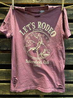 Country Deep Let's Rodeo Bakersfield 1980's Distressed Unisex T shirt vintage wash berry Throw back vintage tee from 1980's 40 Singles Jersey 100% Cotton Premium quality ringspun and compacted cotton Fine Cotton Jersey that is pigment dyed for a more vintage look Features tears and destroyed features at neck and on body Each piece is unique as this process is done by hand! 3.8 oz Made In USA Every garment dye item can be a slightly different shade in color since this is a laundry dye process. En Pink Distressed Graphic Tee, Vintage Distressed Tops For Spring, Vintage Purple Relaxed Fit Tops, Vintage Purple T-shirt With Letter Print, Vintage Purple Graphic Print Top, Vintage Distressed Crew Neck Top, Vintage Distressed Top With Relaxed Fit, Vintage Distressed Tops With Relaxed Fit, Vintage Relaxed Fit Distressed Top