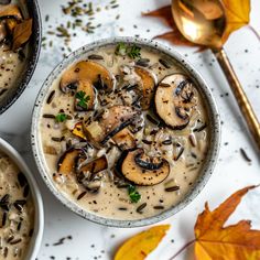 two bowls filled with mushroom soup on top of a white table next to gold spoons