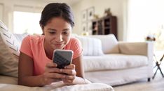 a woman laying on the floor looking at her cell phone while she is reading something