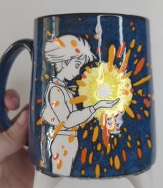 a hand holding a blue coffee mug with yellow and orange sprinkles on it