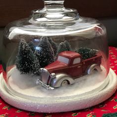 a snow globe with a red truck and trees in it on top of a table