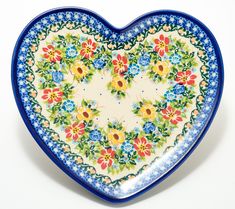 a heart shaped dish with flowers painted on the front and sides in blue, green, yellow and red