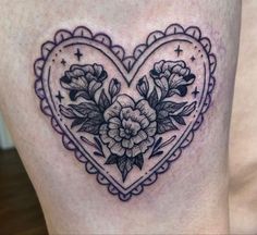 a heart shaped tattoo with flowers on the side of its thigh and an ornate border around it