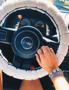 a person driving a car with a steering wheel cover on it's center console