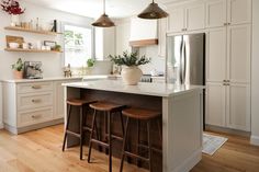 a kitchen with two stools at the center of the island and three lights hanging from the ceiling