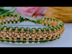 a green and yellow crocheted bracelet with flowers in the background on a white surface