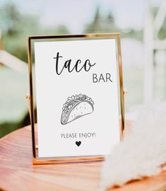 a taco bar sign sitting on top of a wooden table next to a white feather