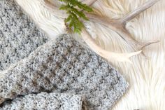 two crocheted hats sitting on top of a white blanket next to a plant