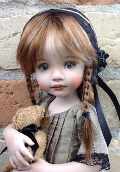 a doll is holding a teddy bear and wearing a black ribbon around her head,