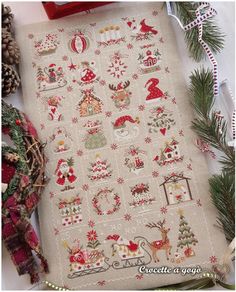 a cross stitch christmas sample on a table next to pine cones and other holiday decorations