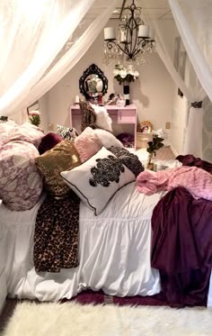 a bed covered in lots of pillows next to a white wall with a chandelier hanging from the ceiling