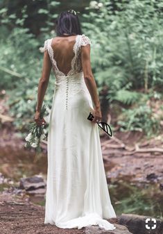 a woman in a white dress is standing on rocks by the river and looking back