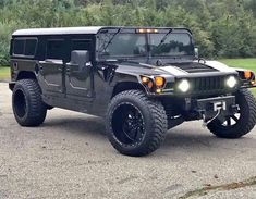 a black hummer truck parked in a parking lot with trees in the back ground