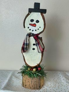 a wooden snowman with a hat and scarf on top of a tree stump in front of a white wall