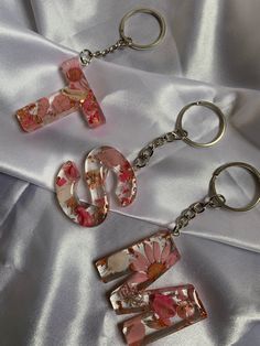 three keychains with flowers on them laying on a white satin surface and one has a flower in the middle